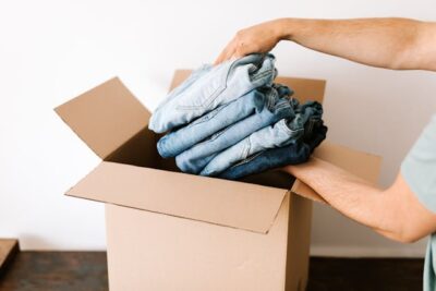 Crop man packing casual clothes into carton box