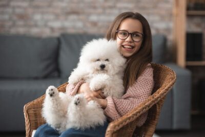 Happy girl in eyeglasses sitting with dog in wicker chair
